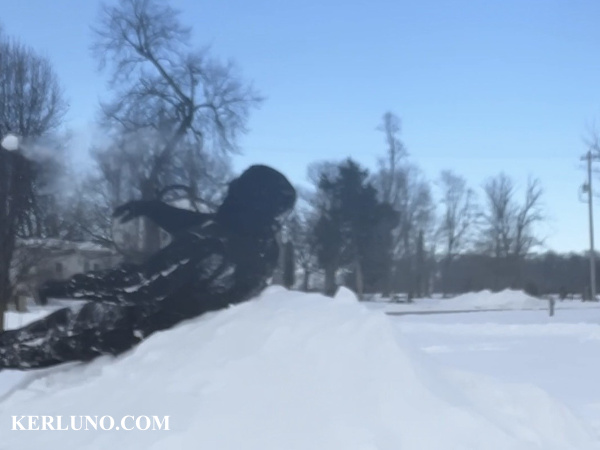 A handsome fella sitting on a pile of snow, throwing a snow ball off-camera.